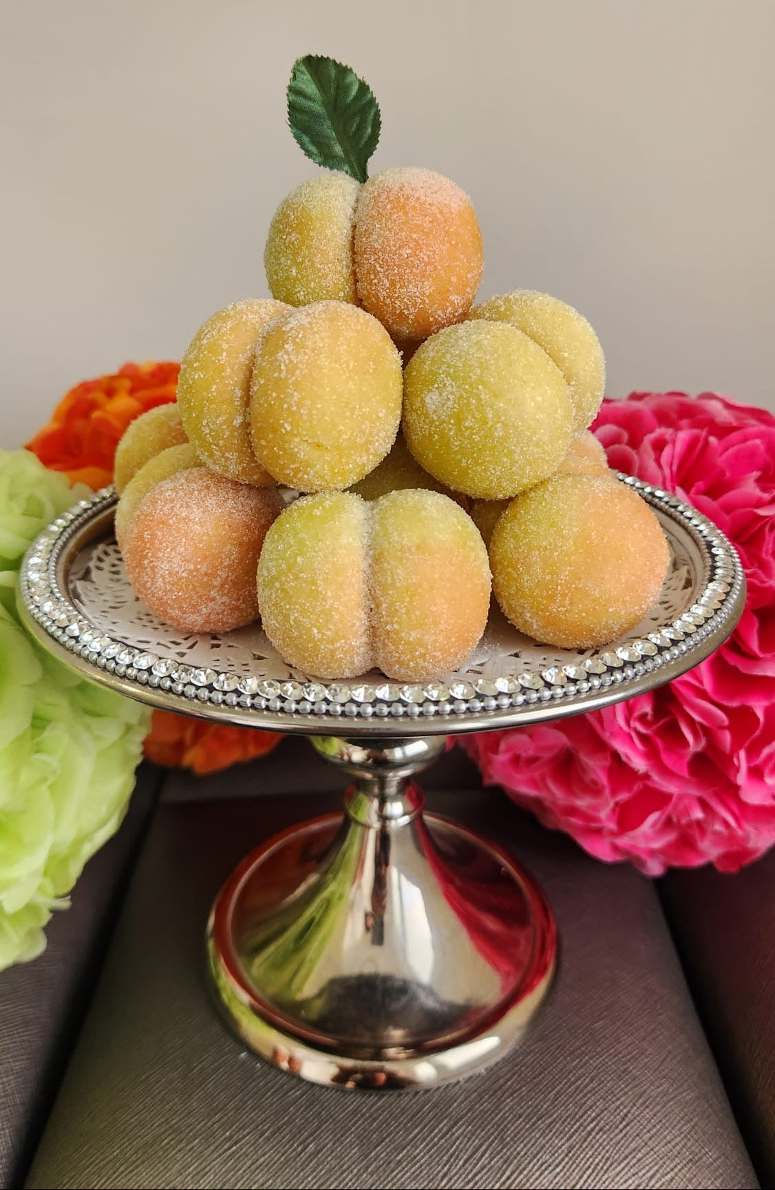 Decorative display of yellow fruits on a silver stand with flowers in the background