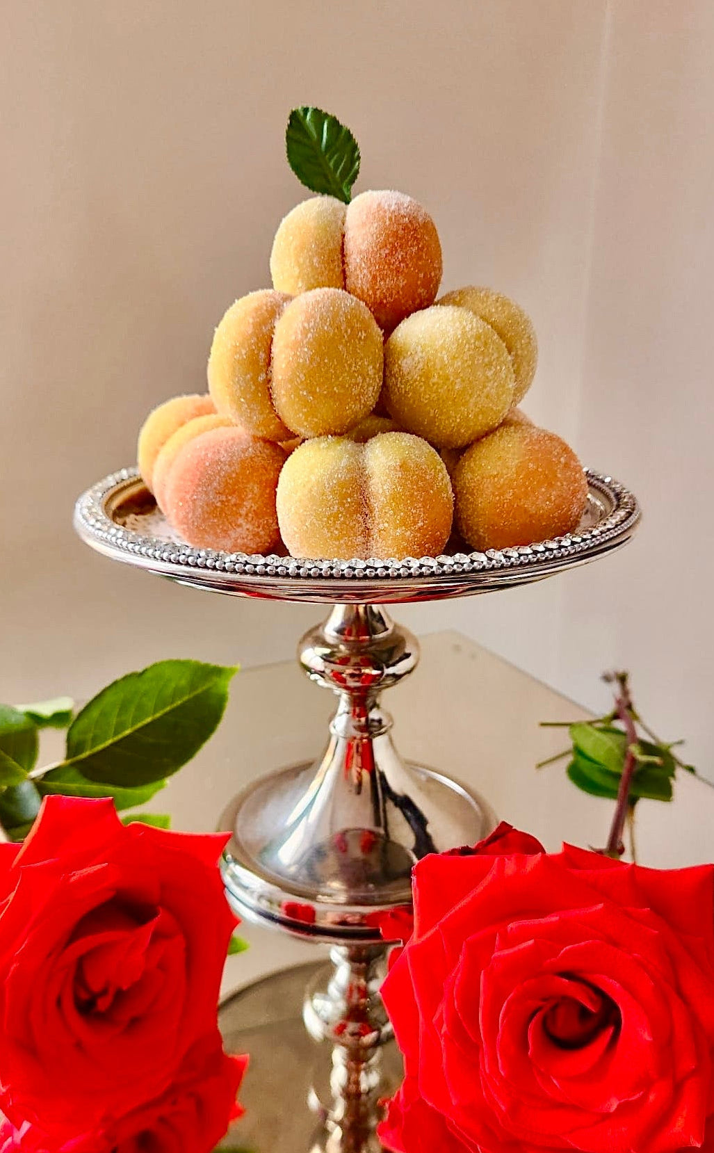 Decorative display of peaches on a silver stand with red roses in the foreground.