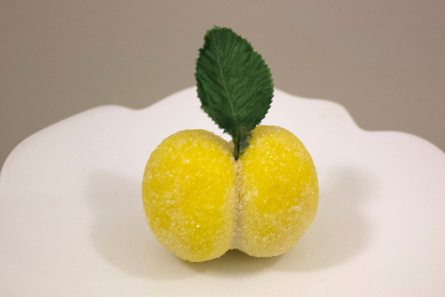 Decorative yellow lemon italian peach cookie with a green leaf on a white plate against a plain background