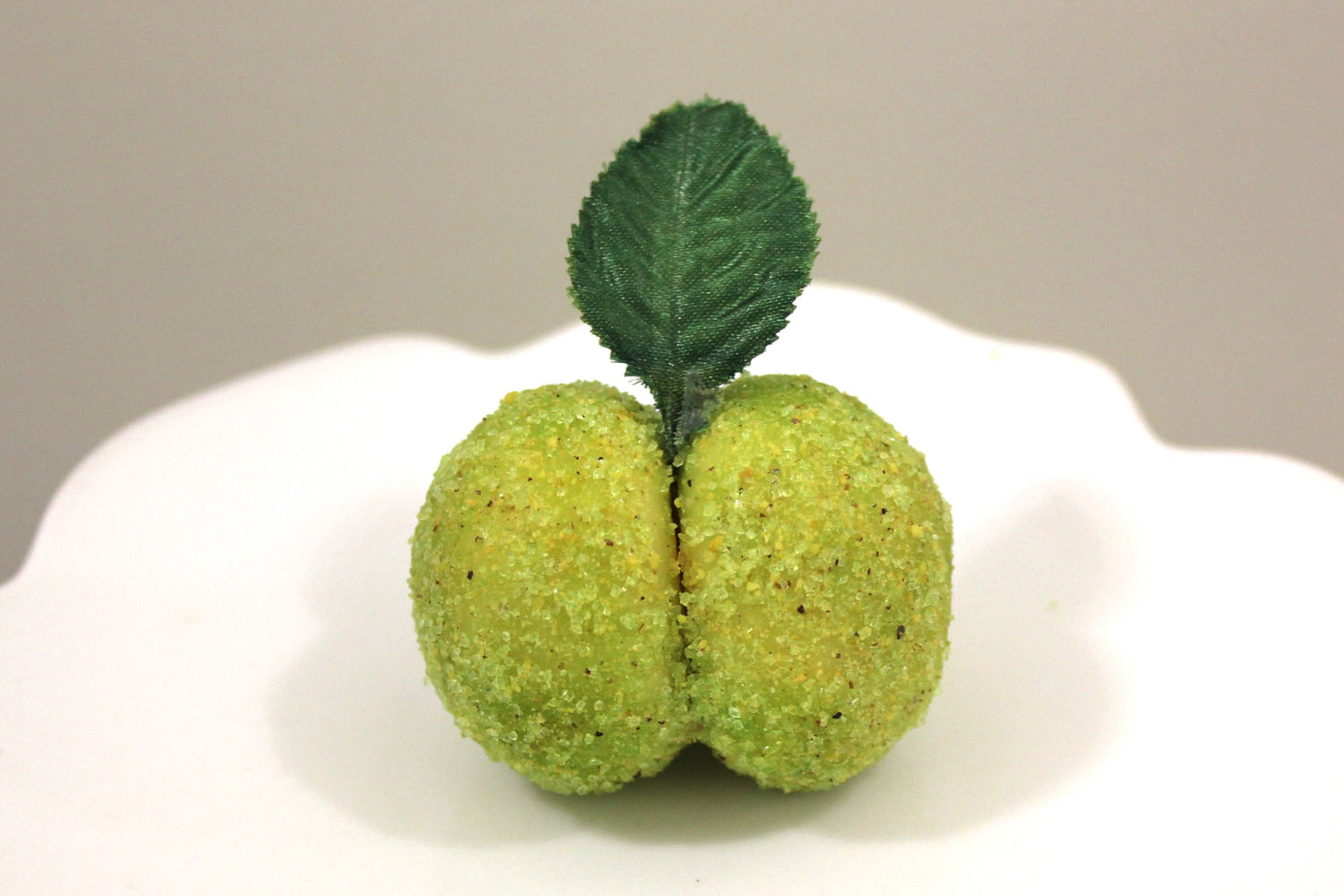 Decorative green pistachio italian peach cookie with  a leaf on a white plate against a plain backround