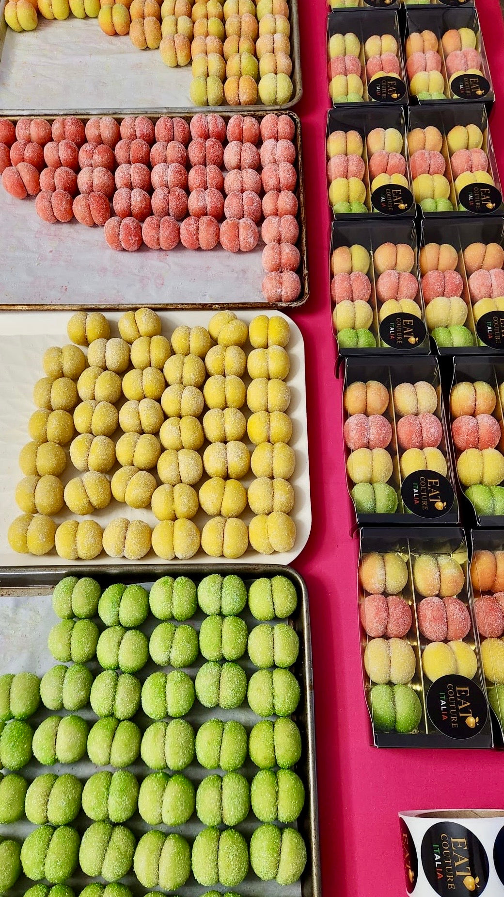 Assorted colorful italian peach cookies in trays on a pink surface
